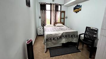 Un dormitorio con una cama, una silla, un calentador, una ventana con cortinas y un cuadro en la pared.