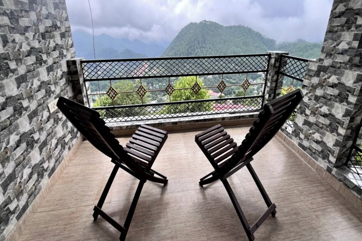A balcony with two wooden chairs, a metal railing, and a view of a mountainous landscape.