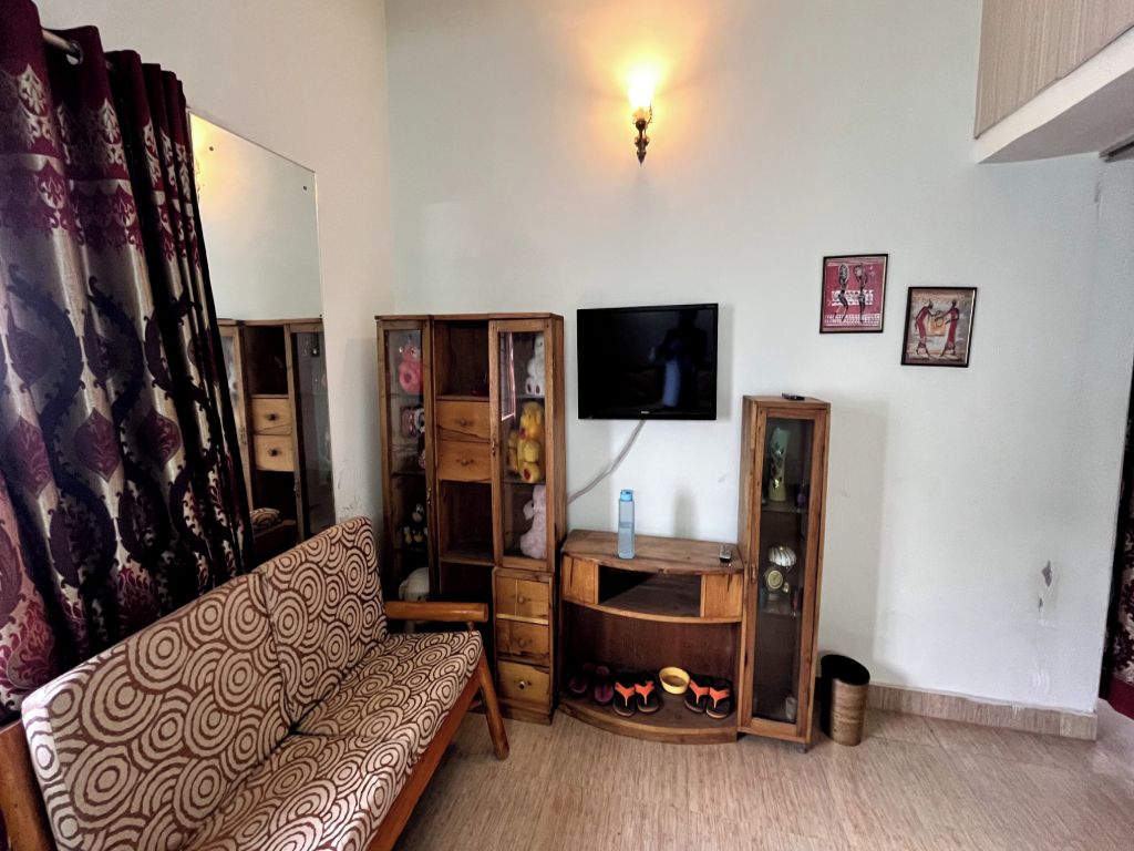 Een woonkamer met een gestreept bankstel, een televisie, houten kasten en een wandlamp.