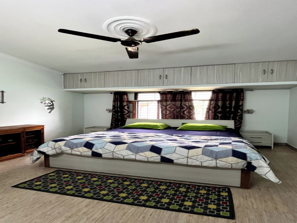 A bedroom with a bed, a ceiling fan, a window with curtains, and a nightstand.