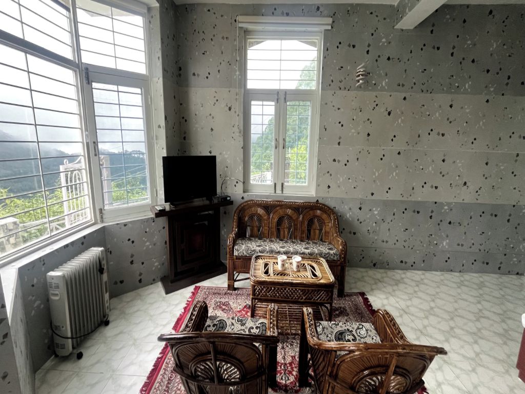 Een kamer met een groot raam, een radiator, een bank, een bijzettafeltje en een televisie.