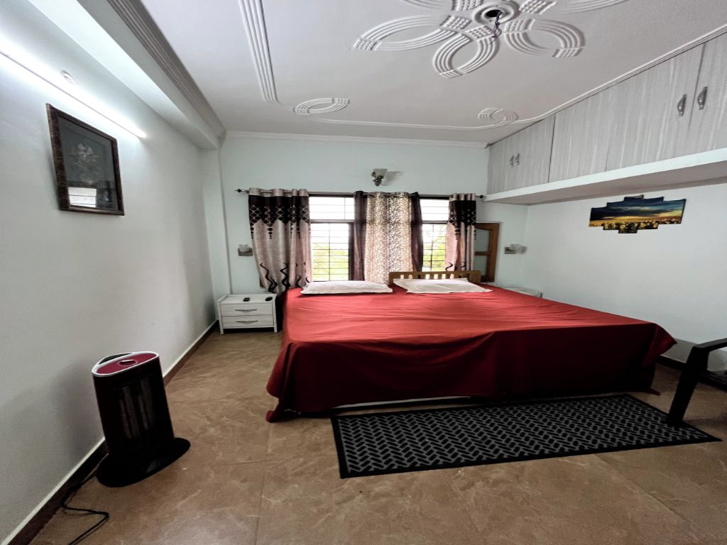 Un dormitorio con cama, un cubo de basura, un radiador y una ventana con cortinas.