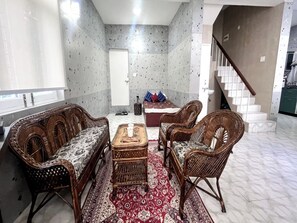 A living room with wicker furniture, a patterned rug, and a staircase leading to an upper floor.