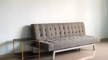 Un sofá moderno con estructura blanca y cabecero tapizado en gris, ubicado frente a una pared lisa en una habitación con piso de baldosas.