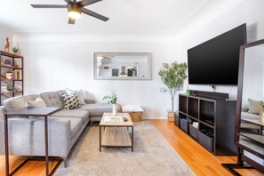 A modern living room with a sectional sofa, a coffee table, a TV, a bookshelf, and a mirror. - West Highlands- walk to Tennyson and Highlands Square (Denver)
