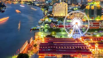 A waterfront cityscape with a prominent Ferris wheel, modern buildings, and a river with moving traffic.