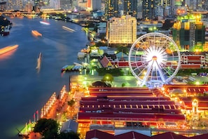 A waterfront cityscape with a prominent Ferris wheel, modern buildings, and a river with moving traffic. - A room Asiatique (Bang Kho Laem)