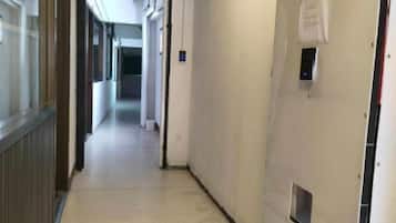 A corridor with a door on the right, a light switch, and a vent on the wall.