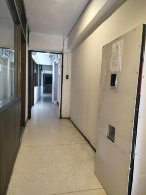 A corridor with a door on the right, a light switch, and a vent on the wall.