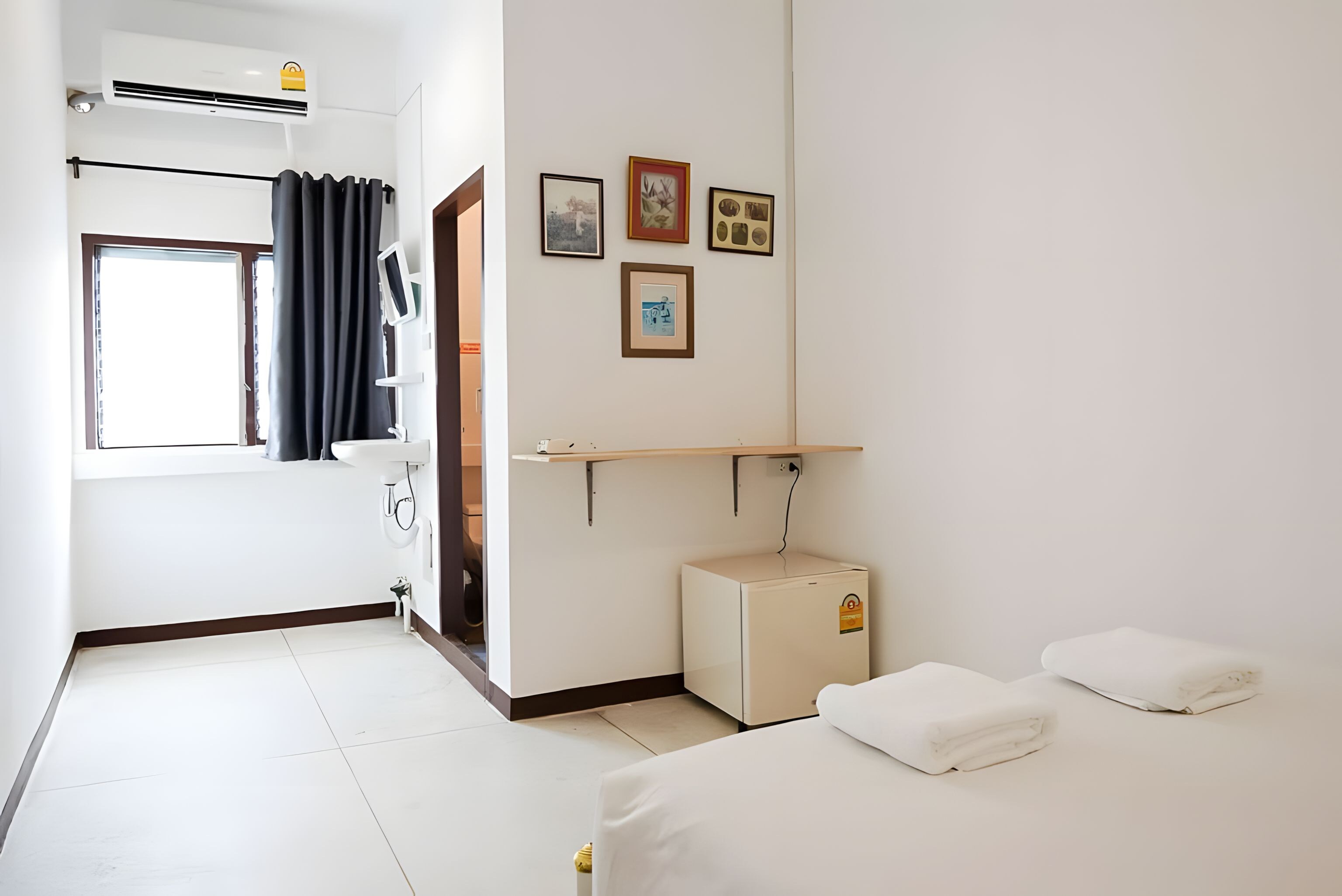 Habitación de hotel con cama, mesita de noche, televisor montado en la pared, refrigerador minibar y ventana con cortinas.