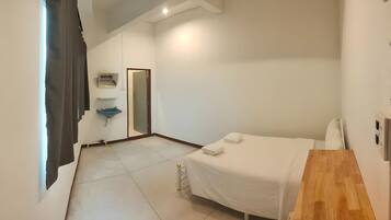 A hotel room with a bed, a wooden desk, a sink, and a mirror.