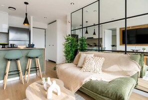 A modern living room with a sofa, a coffee table, and a kitchen area in the background. - Elegante 2BR con piscina y vistas (Miraflores)