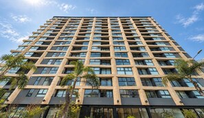 A high-rise building with a grid of windows and balconies, surrounded by palm trees. - Elegante 2BR con piscina y vistas (Miraflores)