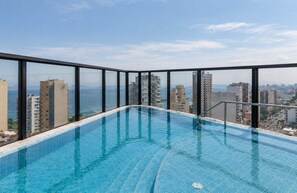 A rooftop infinity pool with a city view, surrounded by glass railings. - Elegante 2BR con piscina y vistas (Miraflores)