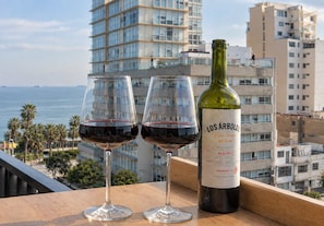 Two wine glasses and a bottle of Los Árboles wine on a balcony with a city view. - Elegante 2BR con piscina y vistas (Miraflores)