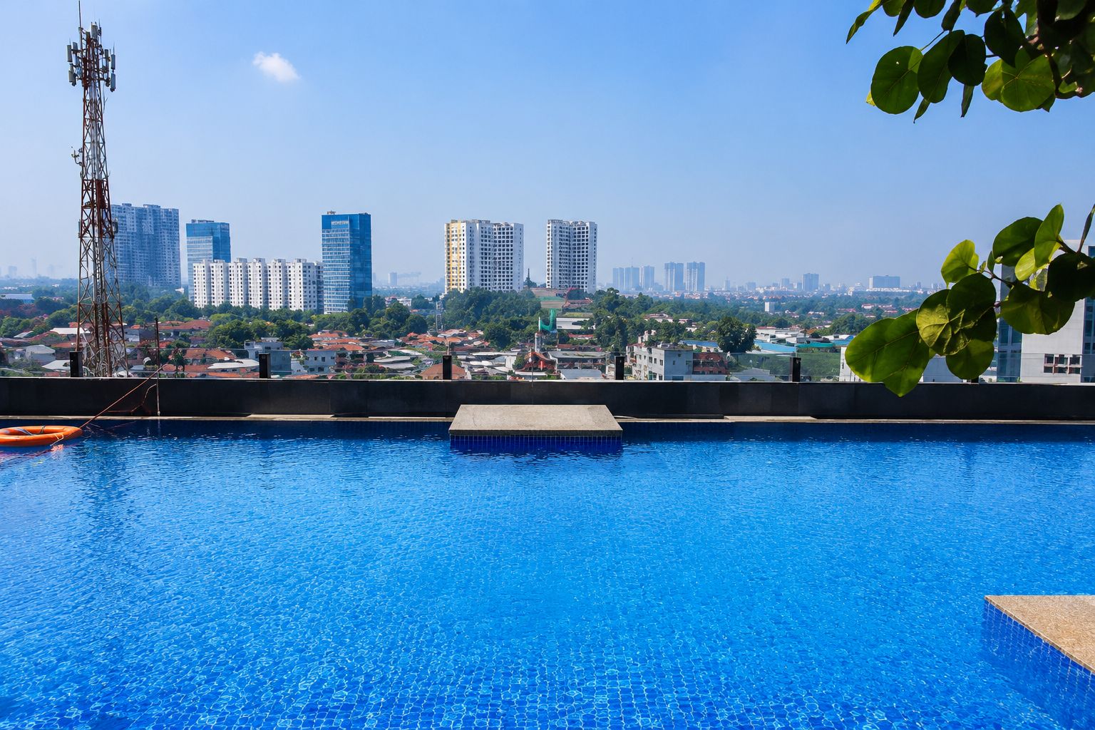 Una piscina con vistas a un paisaje urbano, incluyendo edificios altos y una torre de comunicaciones.