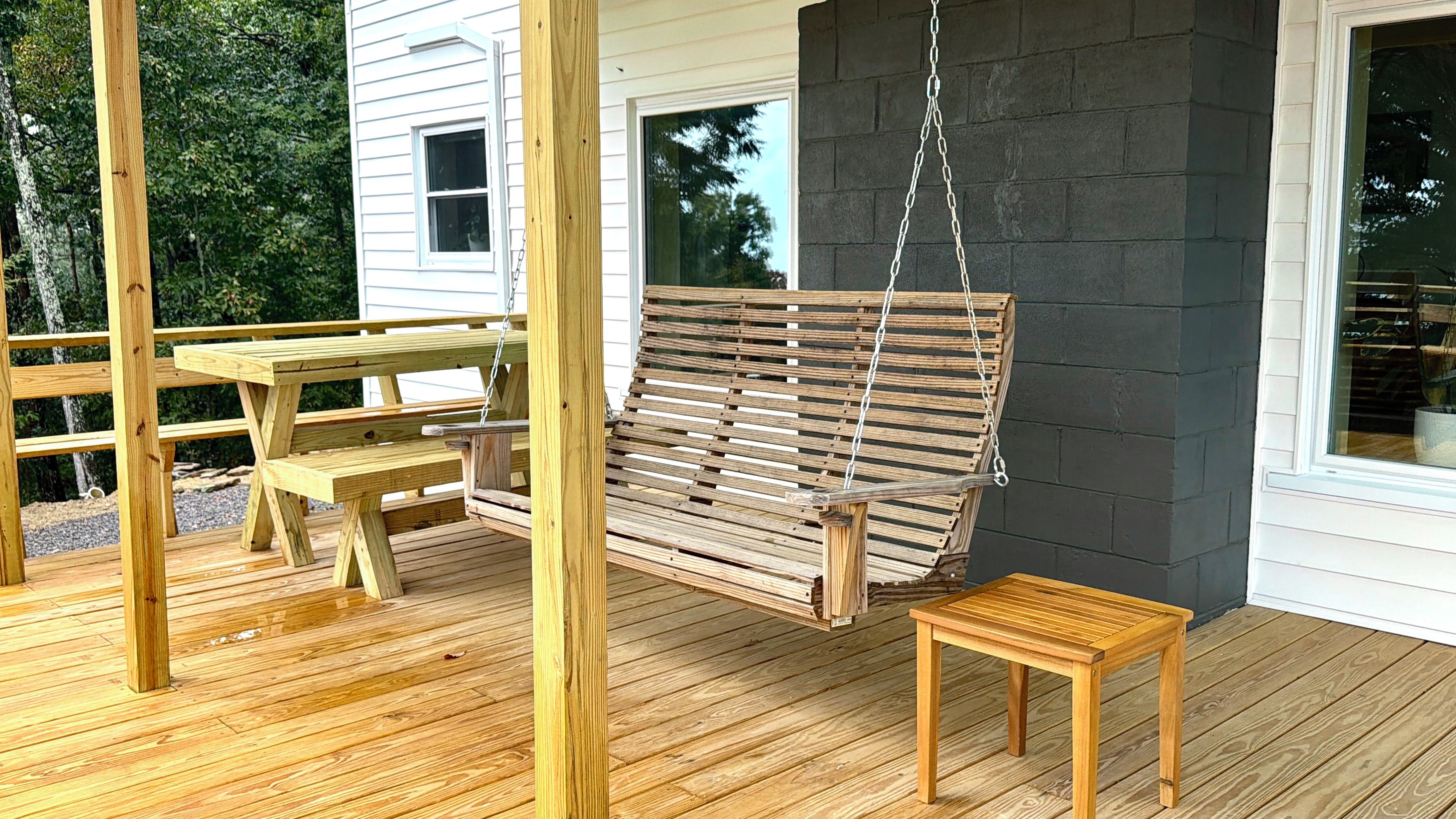 Une terrasse en bois avec une balançoire suspendue, une table de pique-nique et un petit tabouret.
