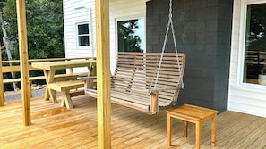 Een houten terras met een hangende schommel, een picknicktafel en een klein krukje.