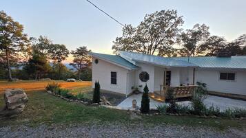 Une maison de plain-pied avec un toit végétalisé, un porche à l’avant et un petit jardin devant, agrémenté d’un muret en pierre et de plantes en pot.