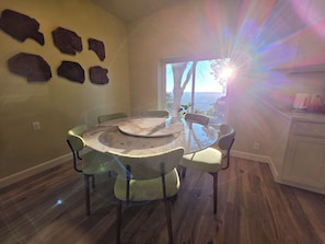 Een eetgedeelte met een ronde tafel, stoelen, uitzicht op de omgeving en een raam.