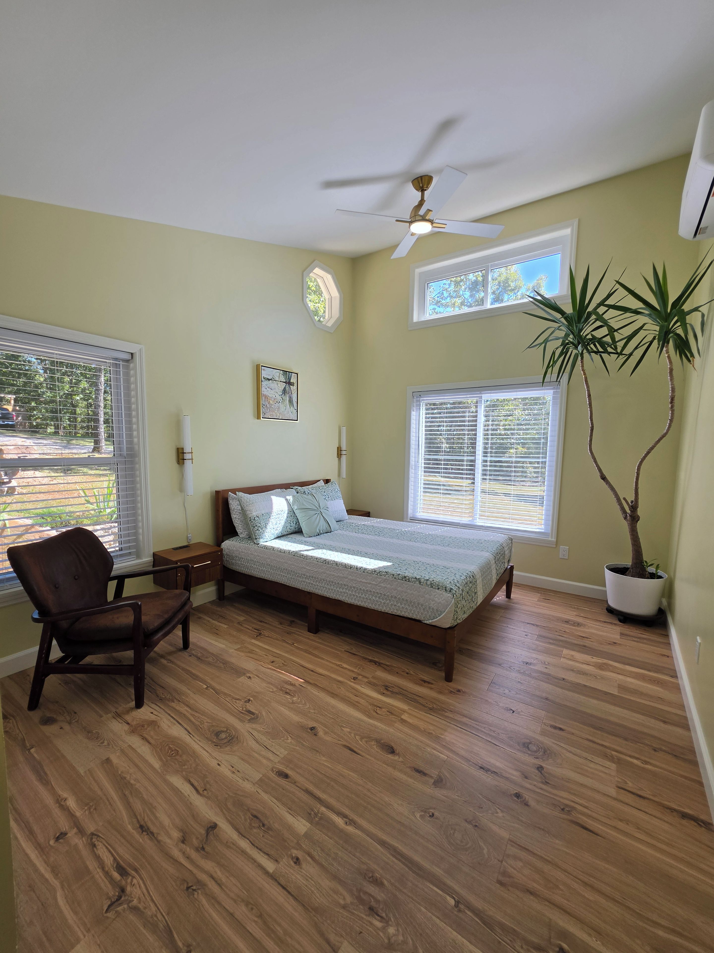 A bedroom with a bed, a chair, a ceiling fan, and a potted plant.