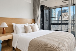 A modern hotel room with a large bed, a nightstand with a lamp, a shower area, and a view of the cityscape through large windows. - Blueground | Jingxin Village, pool, nr Taipei 101 (TPE-14) (Taipei)