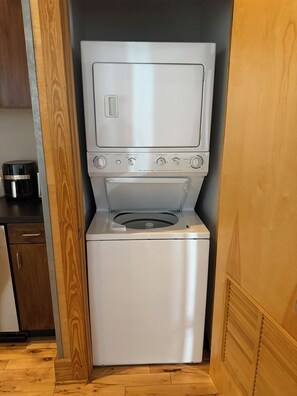Una unitat compacta d'aixelles i assecadora d'acer inoxidable amb panell de control, situada en una habitació amb terres i mobles de fusta.