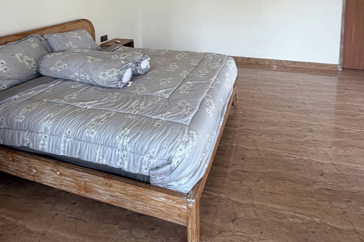 Un dormitorio con cama, cabecera de madera, aire acondicionado instalado en la pared y una puerta de madera.