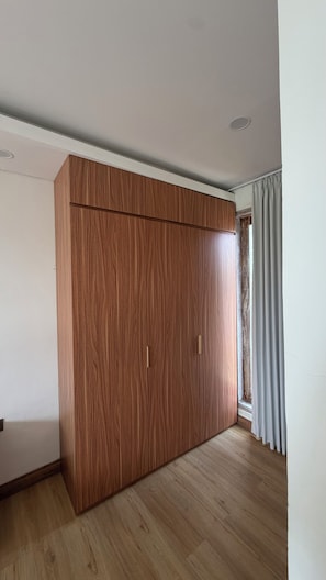 Habitació amb un armari de fusta gran, una finestra amb cortines i un sòl de fusta.