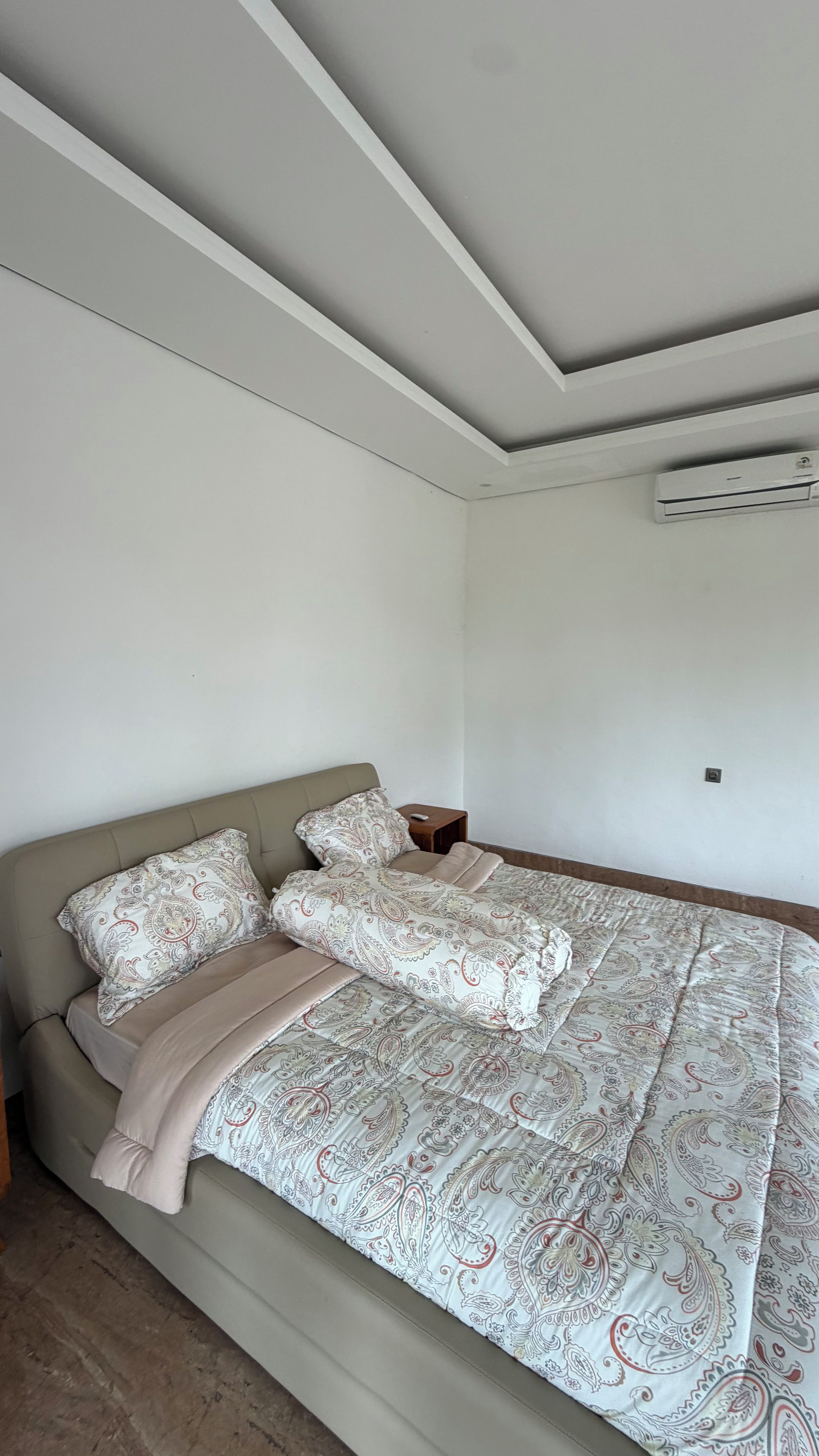 A bedroom with a bed, a nightstand, and an air conditioning unit.