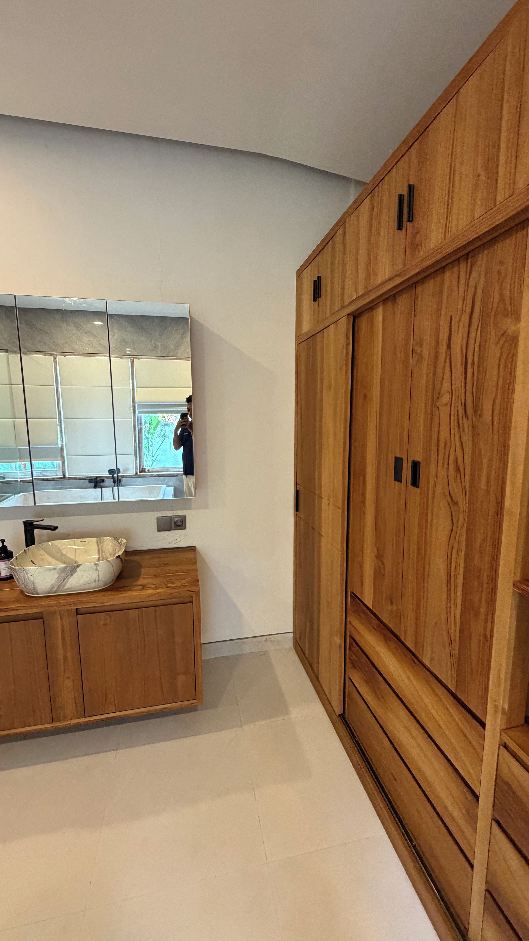 Uma casa de banho moderna com toucador de madeira, um espelho grande e lavatório de mármore.