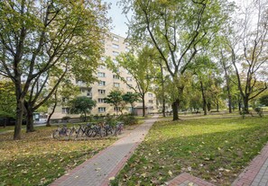 A pathway lined with trees and a building with multiple windows in the background. - Wola Golden Harmony Studio (Warszawa)