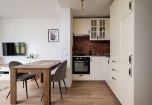 A compact kitchen with white cabinets, a brick backsplash, and a modern stove. - Wola Golden Harmony Studio (Warszawa)