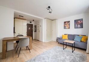 A modern living room with a wooden dining table, a grey sofa with yellow and blue cushions, and a grey shaggy rug. - Wola Golden Harmony Studio (Warszawa)