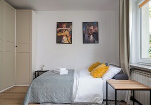 A bedroom with a bed, a bedside table, a nightstand, a window with curtains, and two wall-mounted artworks. - Wola Golden Harmony Studio (Warszawa)