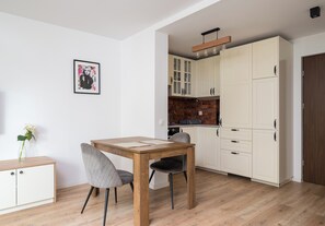 A modern kitchen with white cabinets, a wooden table, and a grey chair. - Wola Golden Harmony Studio (Warszawa)