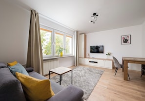 Ett modernt vardagsrum med en grå soffa, ett litet bord, en tv och ett skrivbord i trä.