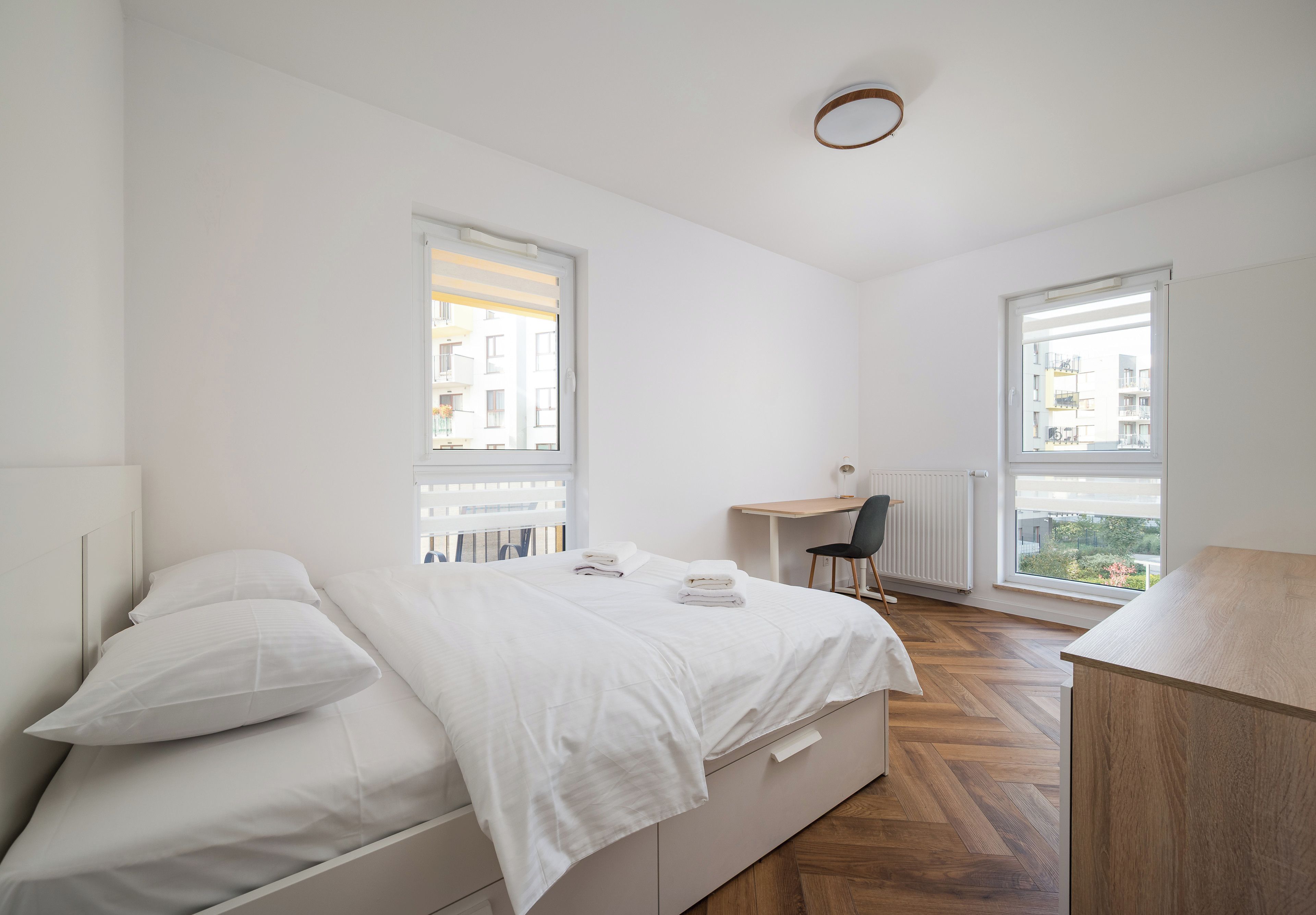 Ein Schlafzimmer mit einem Bett, einem Schreibtisch und zwei Fenstern.