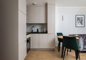 A compact kitchen with a built-in oven, a coffee machine, and a sink. There is a dining area with a table and chairs. - Krochmalna Glamour Apartment (Warszawa)