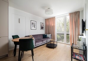 Ein modernes Wohnzimmer mit einer Couch, Sesseln, einem Esstisch und einem großen Fenster.