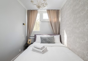 Ein Schlafzimmer mit Bett, Vorhängen, einer Kristallleuchtre und einem Nachttisch mit einem gerahmten Bild.