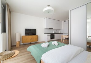 Ein modernes Hotelzimmer mit Bett, Fernseher, Holzschrank, einer Küchenzeile und einem Essbereich.