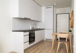 Une cuisine compacte avec des meubles blancs, un plan de travail noir, un four encastré et une petite table avec une chaise.