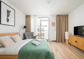 A hotel room with a bed, a chair, a TV, and a window with curtains. - Browary Warszawskie Velvet Studio (Warszawa)