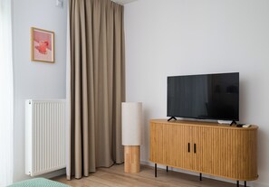 A modern living room with a television on a wooden cabinet, beige curtains, and a radiator. - Browary Warszawskie Velvet Studio (Warszawa)