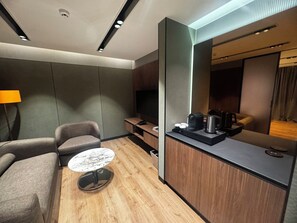 Habitación de hotel moderna con sofá, una pequeña mesa redonda, televisor, estación de café y espejo.