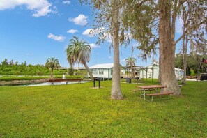 A grassy area with picnic tables, a small pond, and a building with a white roof.