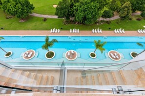 A rooftop pool with sun loungers and palm trees, surrounded by a well-maintained lawn and a golf course. - Airbnb Be Sky Top | 1BR with Private Rooftop (Bavaro)