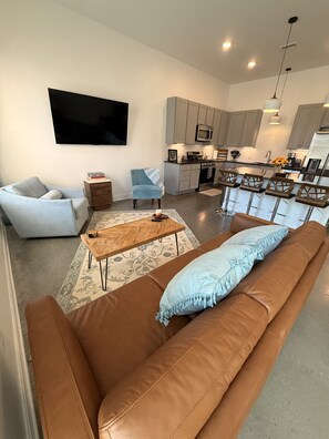 Una sala moderna con un sofá de cuero marrón, un sillón azul claro y una mesa de centro de madera.