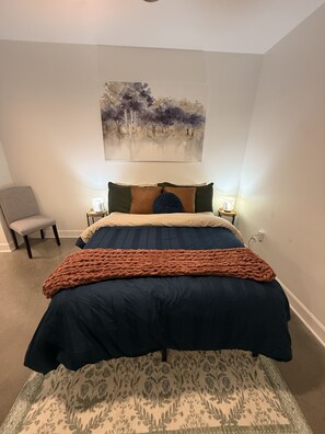 A bedroom with a bed, a chair, a painting, and bedside lamps. - *NEW* Lawrencian Loft 2BD/BA- Blocks from Mass! (Lawrence)